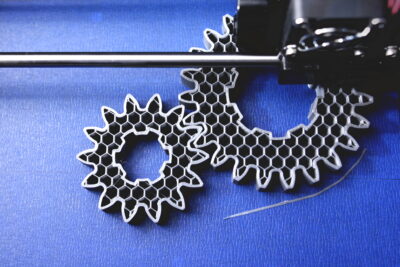 FDM 3D-printer manufacturing spur gears from silver-gray filamen