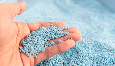 Hand on large pile of blue plastic granules in temporary storage
